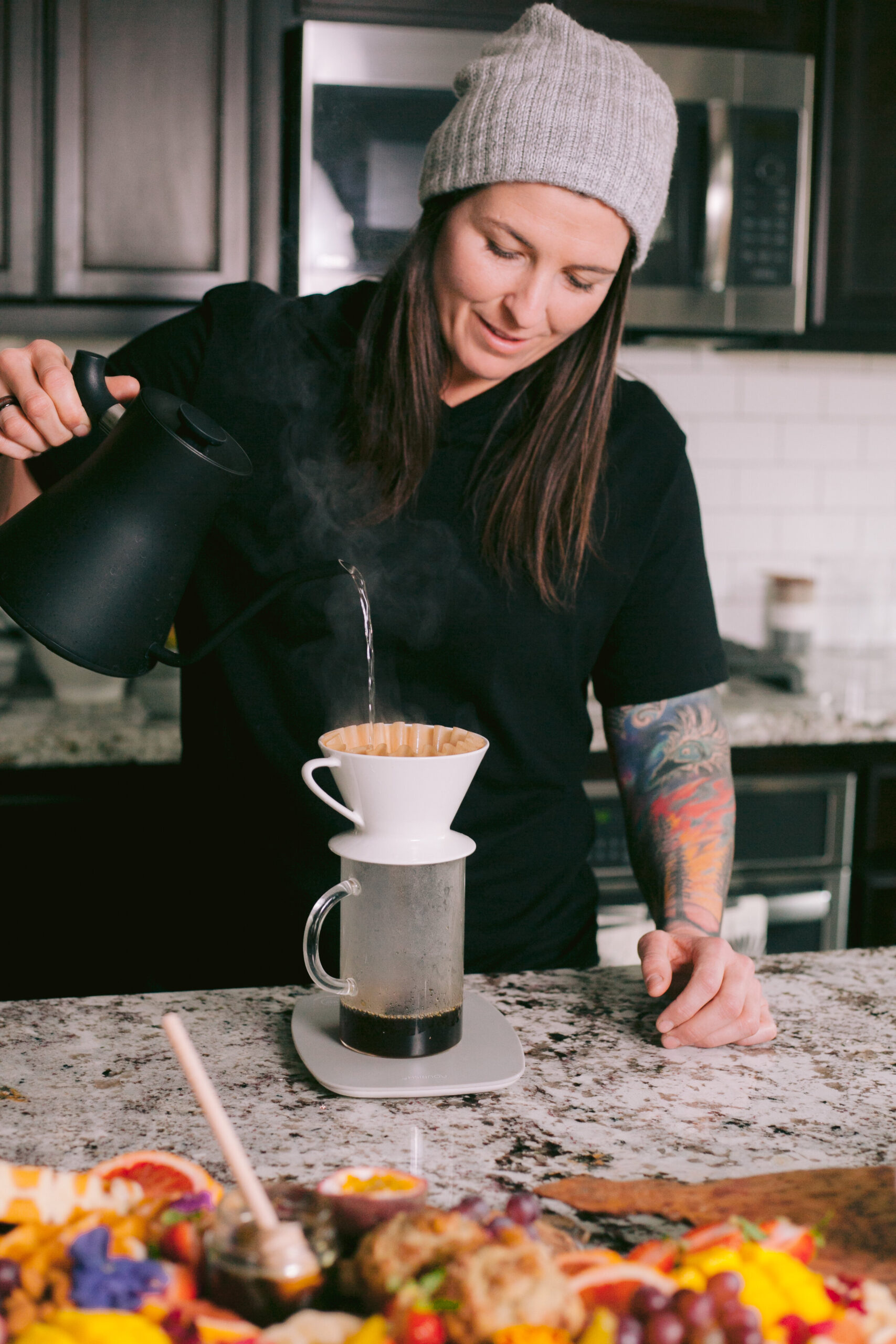  Woman pouring hot water over pour over brewer in kitchen.  