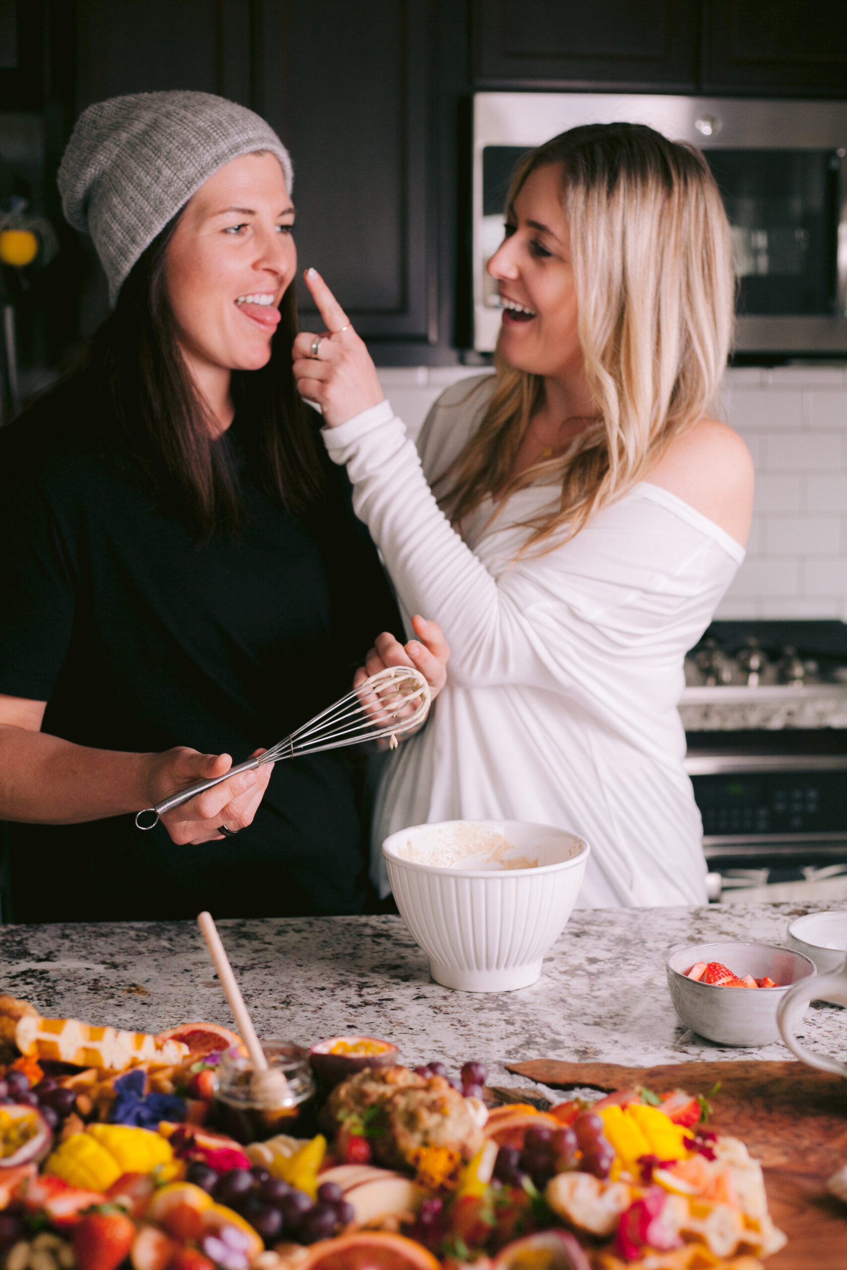 Blonde woman touched brunette woman on the nose with waffle batter