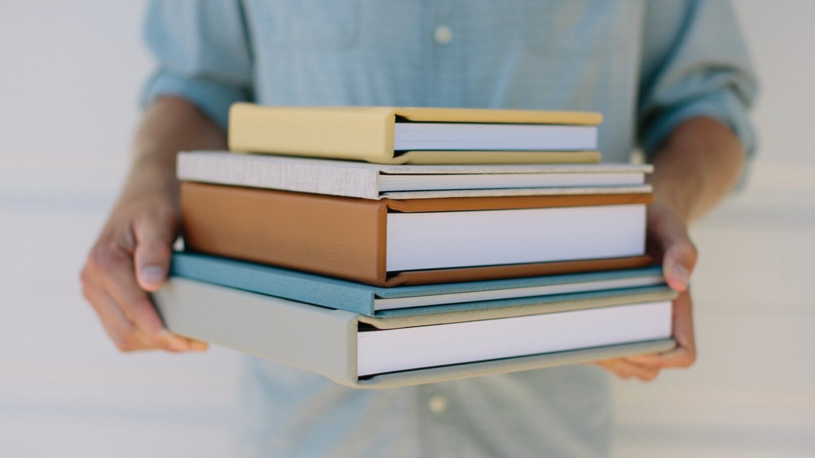 Man holding a stack of 5 different photo albums